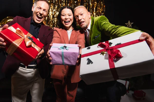 Gifts with confetti in hands of blurred interracial friends on black background — Stock Photo