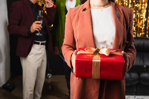 Vista ritagliata di donna in possesso di scatola regalo con coriandoli vicino amici offuscati su sfondo nero — Foto stock