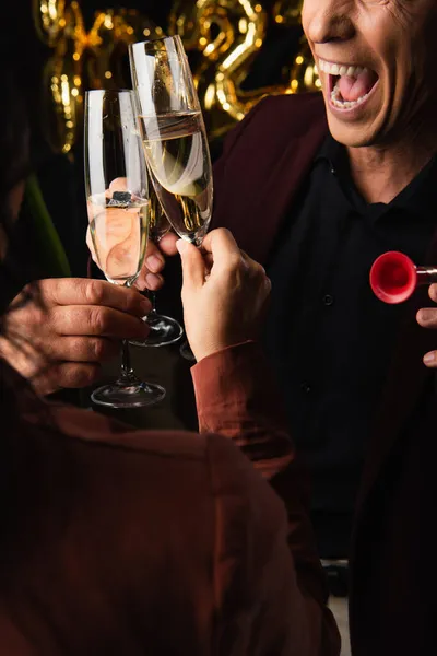 Corte vista de animado homem com festa chifre clinking champanhe com amigos no preto fundo — Fotografia de Stock