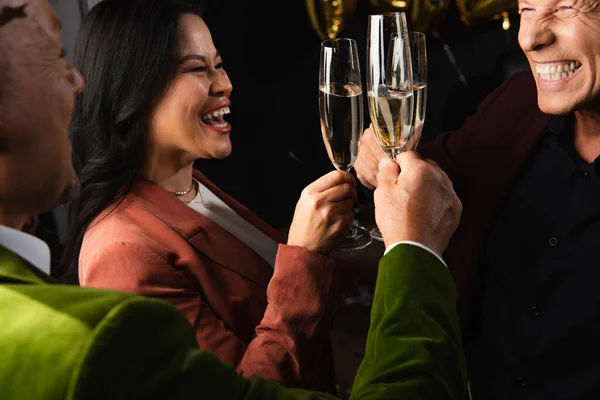 Позитивные межрасовые друзья пьют шампанское во время новогодней вечеринки на черном фоне — стоковое фото