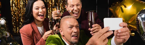 Älterer Mann macht Selfie mit interrassischen Freunden, die Champagner während der Neujahrsparty auf schwarzem Hintergrund halten, Banner — Stockfoto