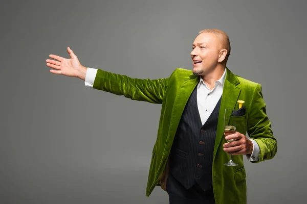 Positive man with glass of champagne pointing with hand and looking away isolated on grey — Stock Photo