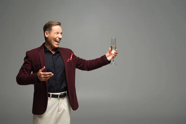 Hombre positivo en ropa formal apuntando a la copa de champán aislado en gris - foto de stock