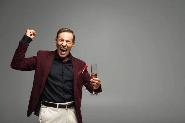 Homme mûr excité avec verre de champagne montrant oui geste isolé sur gris — Photo de stock