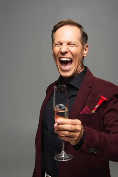 Homme mûr excité avec corne de fête et champagne regardant la caméra isolée sur gris — Photo de stock