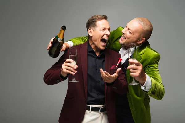 Excited mature men in formal wear holding champagne and bottle isolated on grey — Stock Photo