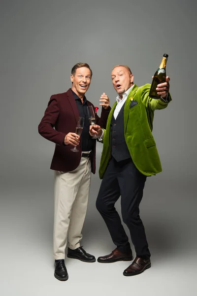 Excited mature men with champagne and bottle looking at camera on grey background — Stock Photo