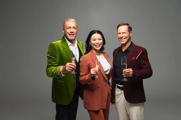 Des amis multiethniques souriants avec des verres de champagne regardant la caméra isolée sur gris — Photo de stock