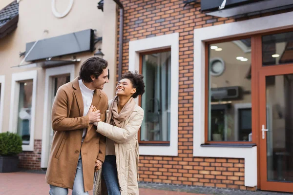 Alegre africana americana mujer cogida de la mano mientras caminando con novio al aire libre - foto de stock