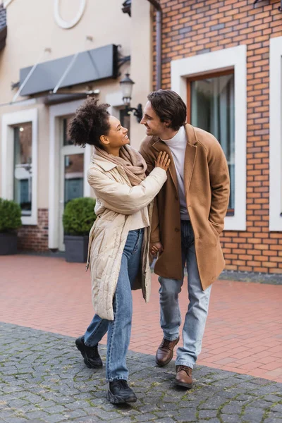 Longitud completa de la alegre mujer afroamericana cogida de la mano mientras está de pie con su novio al aire libre - foto de stock