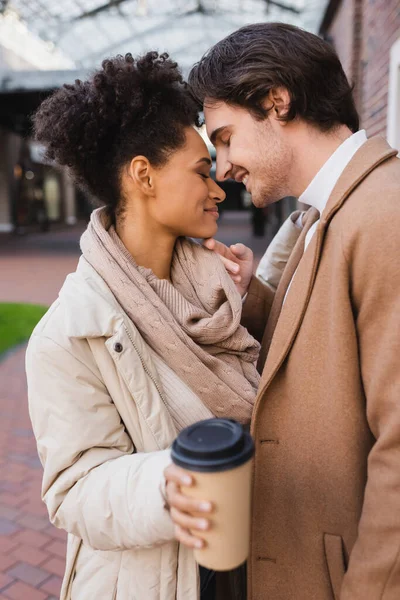 Feliz afroamericana mujer sosteniendo borrosa taza de papel con café para ir cerca de novio - foto de stock