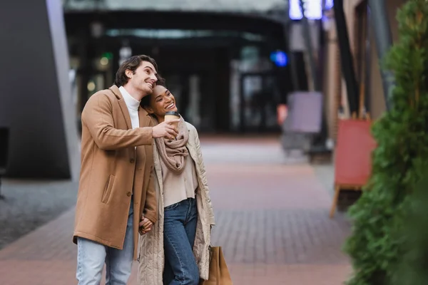 Africano americano donna holding shopping bags vicino felice fidanzato in cappotto in centro commerciale — Foto stock