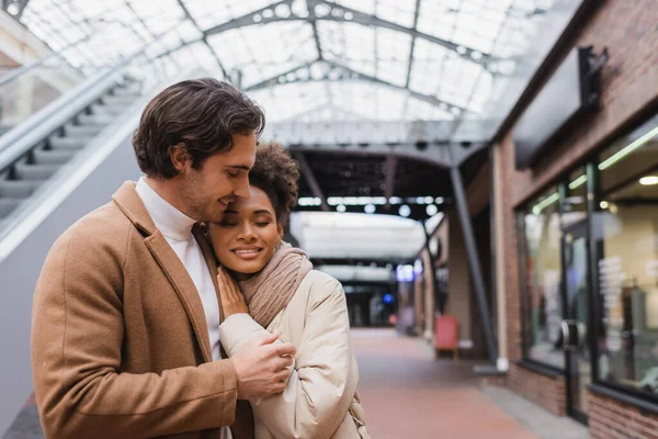 Alegre pareja interracial sonriendo en el centro comercial - foto de stock