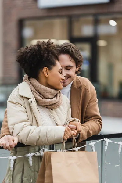 Happy man holding hands with smiling african american girlfriend in shopping mall — Stock Photo