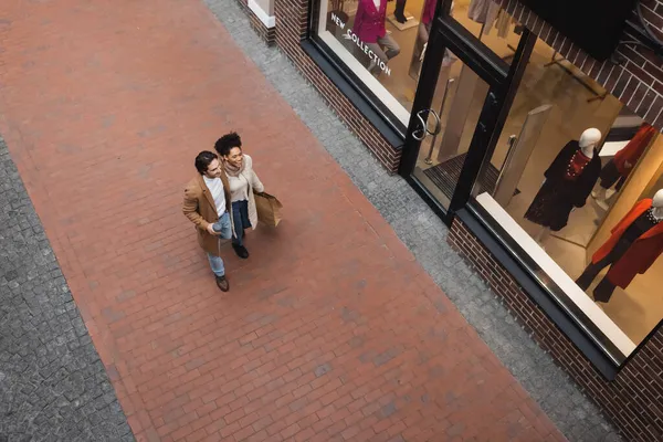 Vista dall'alto di felice coppia interrazziale con acquisti a piedi nel centro commerciale — Foto stock