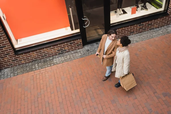 High angle view of joyful interracial couple with purchases walking in mall — Stock Photo