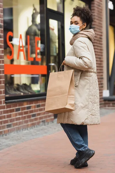 Brunette african american woman in medical mask doing christmas shopping in mall — Stock Photo