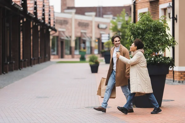 Alegre afroamericana mujer apuntando con el dedo cerca novio mientras caminando cerca de centro comercial — Stock Photo