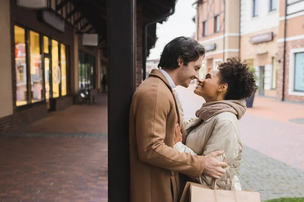 Side view of cheerful african american woman hugging boyfriend with shopping bags — Stock Photo