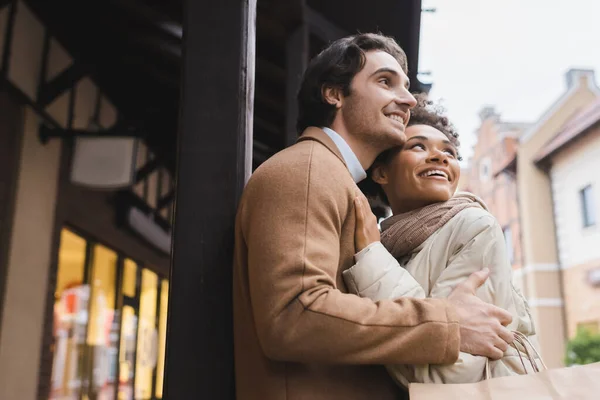 Low angle view of excited interracial couple hugging near mall — Stock Photo