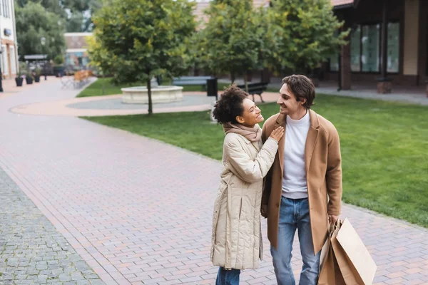 Glücklich afrikanisch-amerikanische Frau umarmt fröhlichen Freund mit Einkaufstüten draußen — Stockfoto