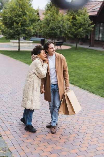 Feliz africana americana mujer abrazando alegre novio con compras bolsas fuera - foto de stock