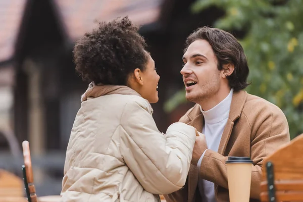 Asombrada pareja interracial en abrigos tomados de la mano - foto de stock