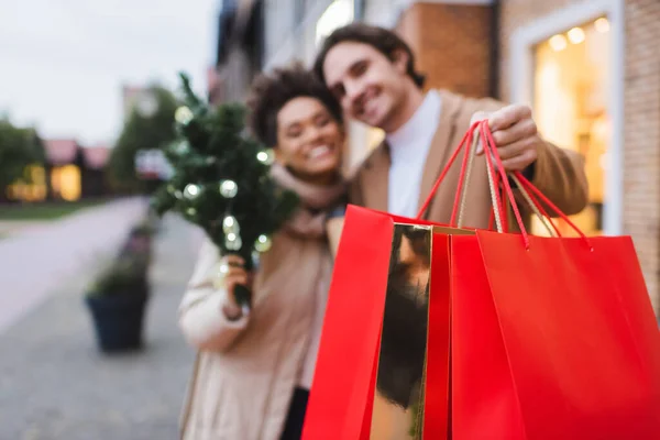 Casal interracial desfocado com sacos de compras de Natal perto do shopping — Fotografia de Stock