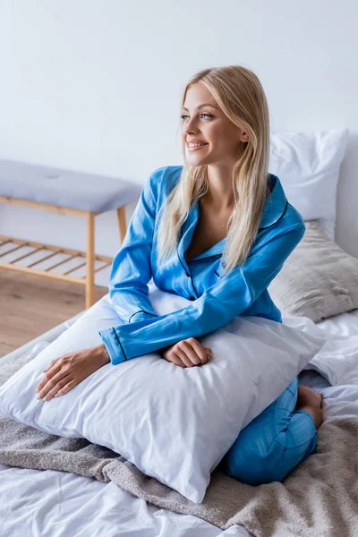 Sorrindo jovem segurando travesseiro enquanto sentado na cama — Fotografia de Stock