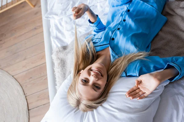 Draufsicht auf glückliche blonde Frau, die auf Kissen im Schlafzimmer liegt — Stockfoto