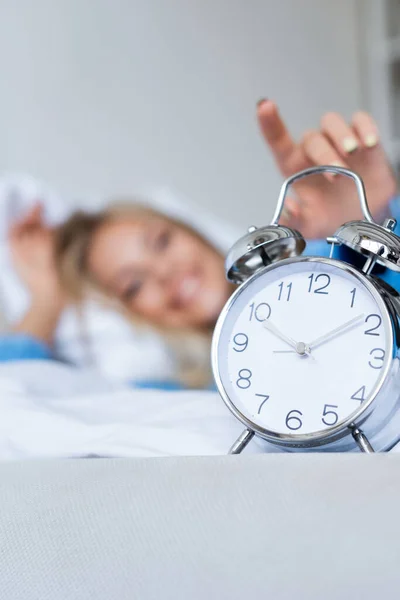 Mujer feliz y borrosa alcanzando despertador retro - foto de stock