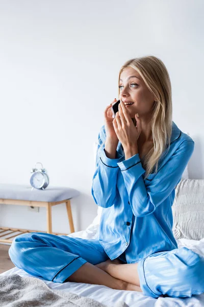 Mujer sorprendida en pijama hablando en smartphone en el dormitorio - foto de stock