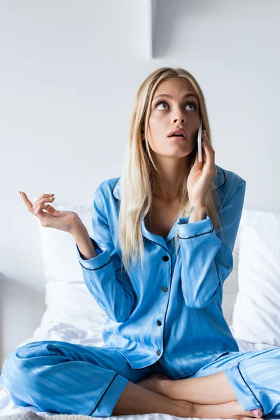 Pensive woman in pajamas talking on smartphone in bedroom — Stock Photo