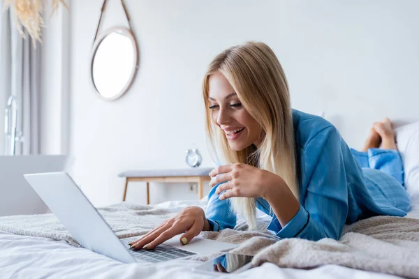 Happy young freelancer in pajamas using laptop in bedroom — Stock Photo