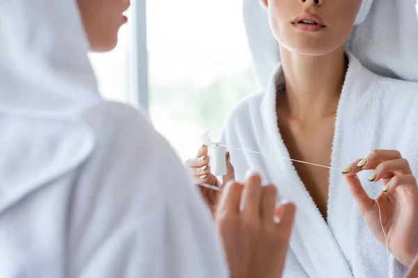 Vista recortada de la mujer joven sosteniendo hilo dental cerca del espejo - foto de stock