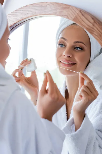 Young and cheerful woman in bathrobe holding dental floss near mirror — Stock Photo