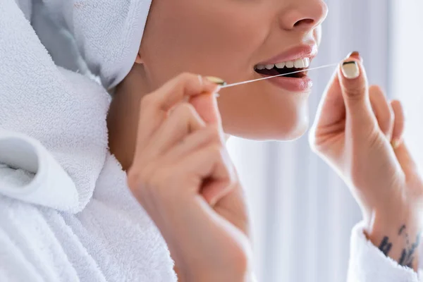 Vista recortada de mujer joven tatuada sosteniendo hilo dental en el baño - foto de stock