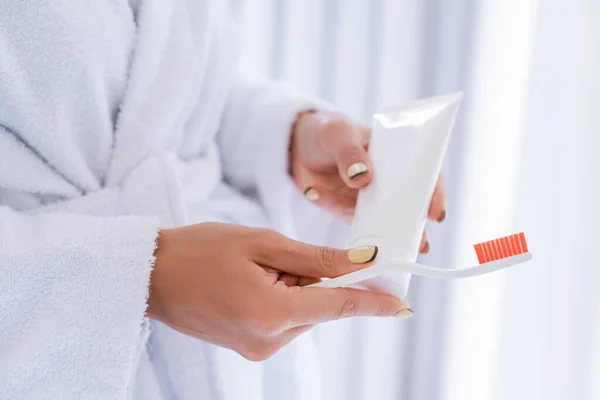 Vista parziale di giovane donna in possesso di spazzolino da denti e dentifricio tubo in bagno — Foto stock