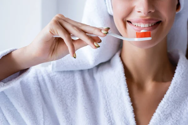 Обрезанный вид молодой улыбающейся женщины, чистящей зубы в ванной комнате — стоковое фото