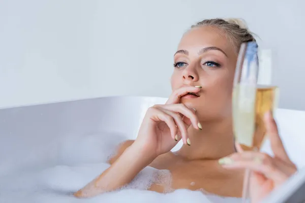 Молодая мечтательная женщина принимает ванну и держит размытый бокал шампанского — стоковое фото