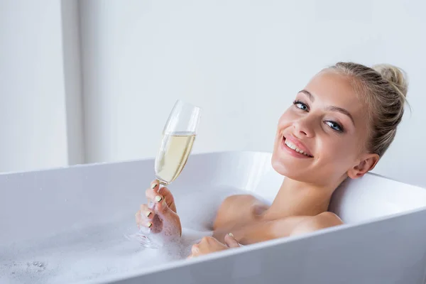 Mujer joven y alegre tomando baño y sosteniendo una copa de champán - foto de stock