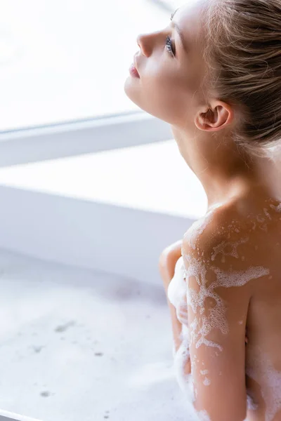 Mulher jovem e molhada com espuma no corpo tomando banho — Fotografia de Stock