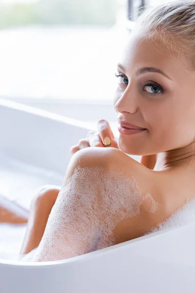 Pleased young and wet woman with foam on body taking bath — Stock Photo