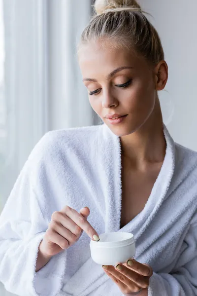 Young woman in bathrobe holding container with cosmetic cream — Stock Photo