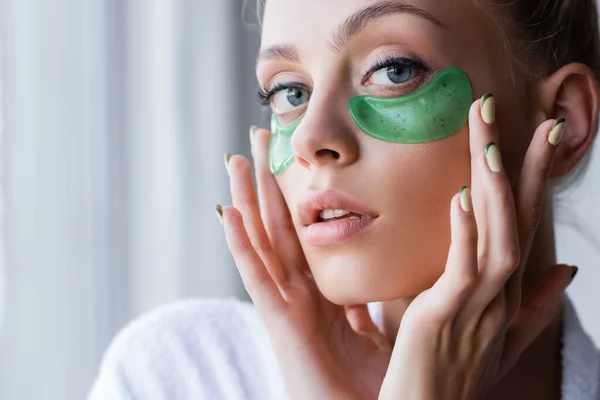 Young woman in bathrobe applying eye patches in bathroom — Stock Photo