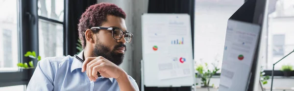 Uomo d'affari afroamericano con gli occhiali che guarda il monitor del computer in ufficio, striscione — Foto stock