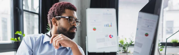 Hombre de negocios afroamericano en anteojos mirando el monitor de computadora en la oficina, pancarta - foto de stock