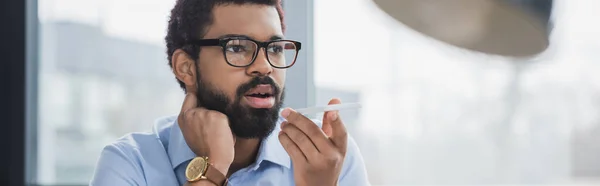 African american businessman in eyeglasses recording voice message on smartphone, banner — Stock Photo