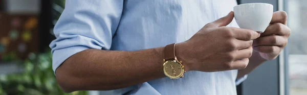 Vista ritagliata di uomo d'affari afro-americano in abbigliamento formale in possesso di tazza di caffè, banner — Foto stock