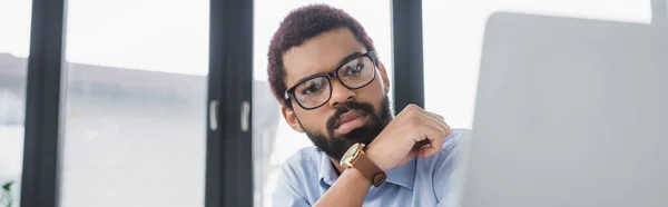 Jeune gestionnaire afro-américain à la recherche d'un ordinateur portable flou dans le bureau, bannière — Photo de stock